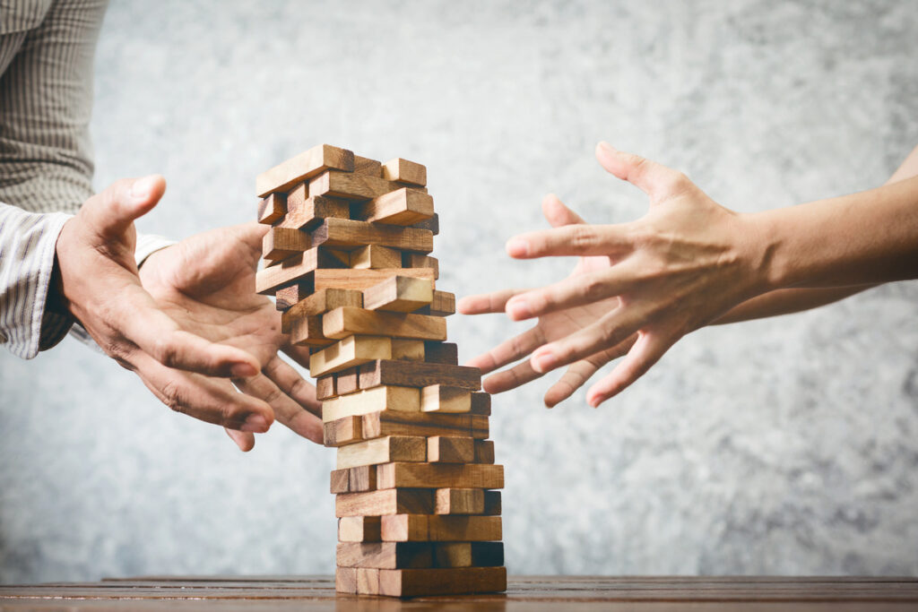 Two people trying to catch a falling Jenga tower
